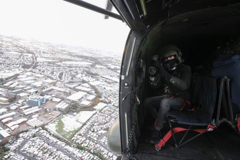 Filming from an open helicopter door over a snow-covered town