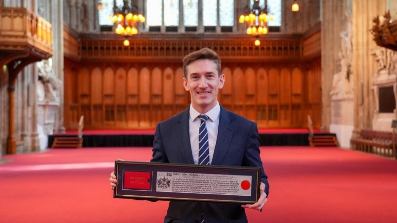 Robert Midgley holding his framed Freedom of the City of London certificate in a great hall